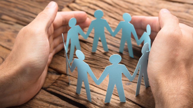 Cropped image of businessman's hands covering paper team on wooden table